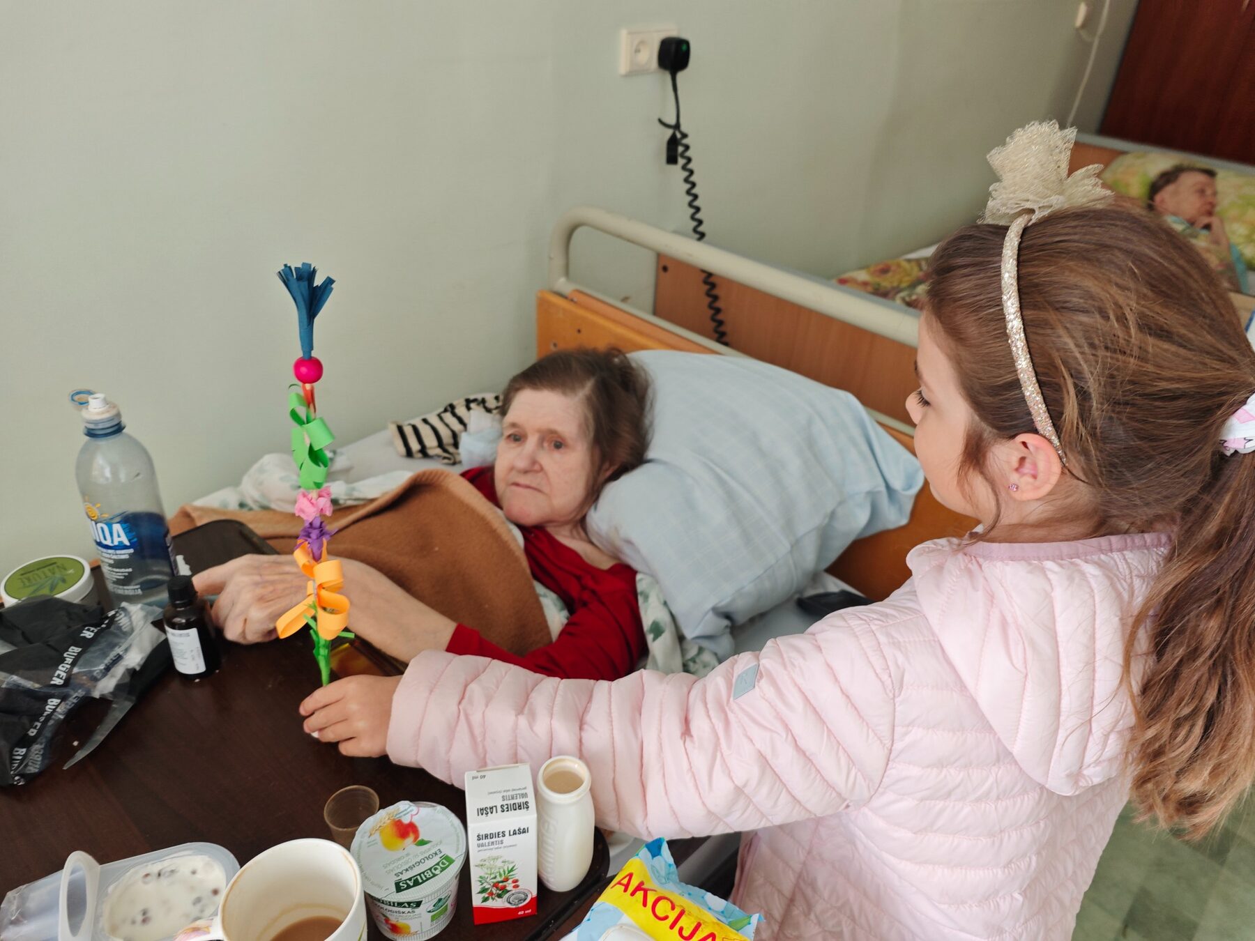 Mergaitė įteikia globos namų gyventojai pačios pagamintą gėlę